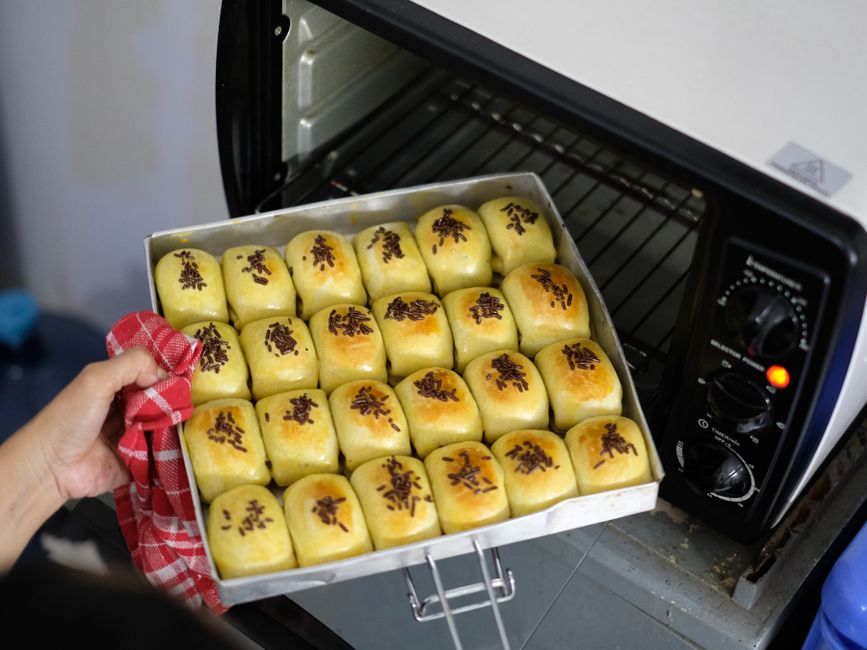 A tray of freshly baked buns being taken out of a home oven.